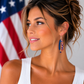 Model wearing handcrafted red, white and blue asymmetrical polymer clay earrings with silver chain accents from Claybella Studio.