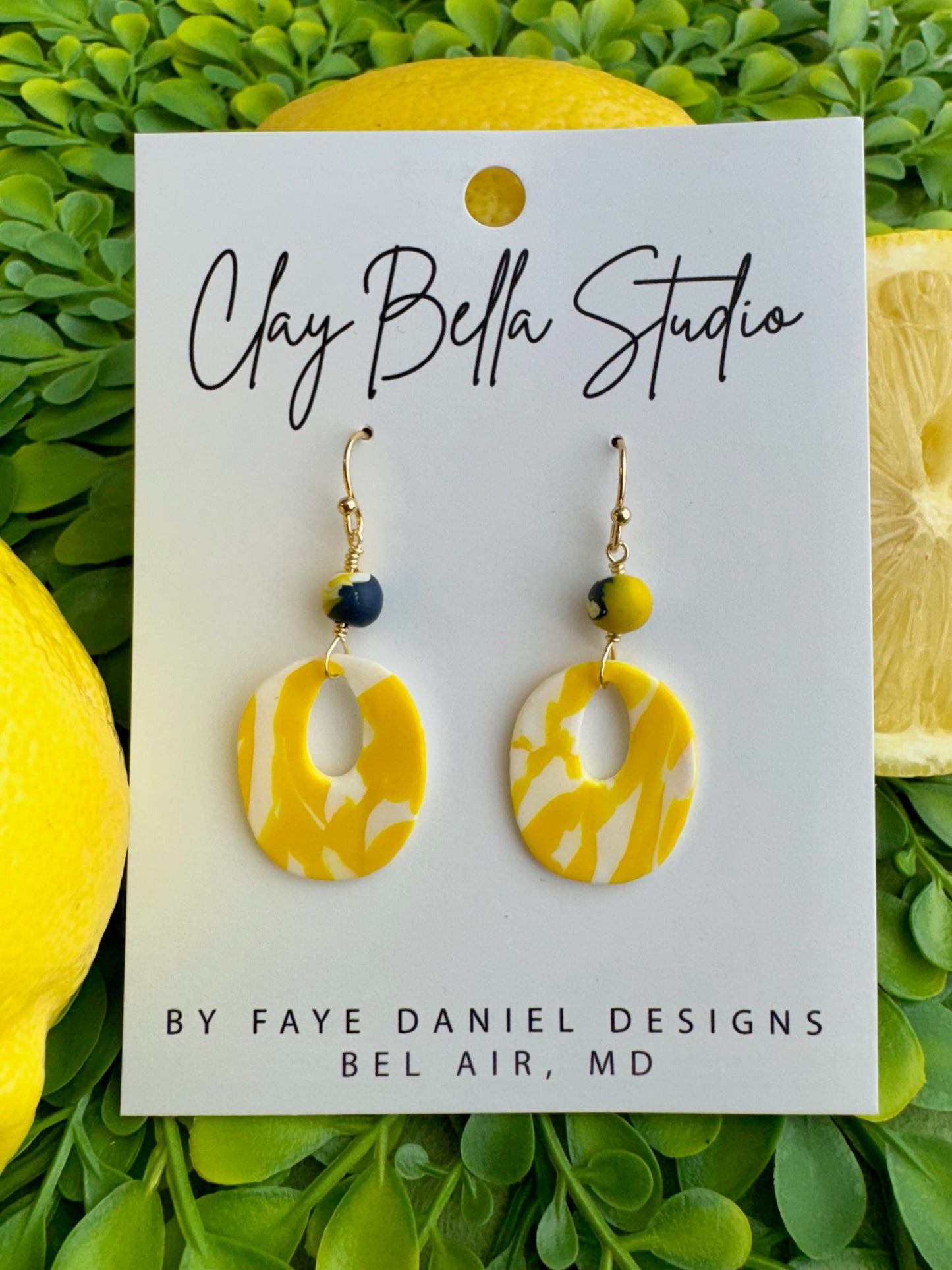 Yellow and white marbled polymer clay drop earrings with hypoallergenic gold ear wires. Claybella Studio with greenery and lemons behind card.