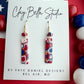 Handmade red, white and blue mosaic polymer clay rectangle earrings with gold and silveer foil. A handmade matching matching bead on Clay Bella Studio display card.