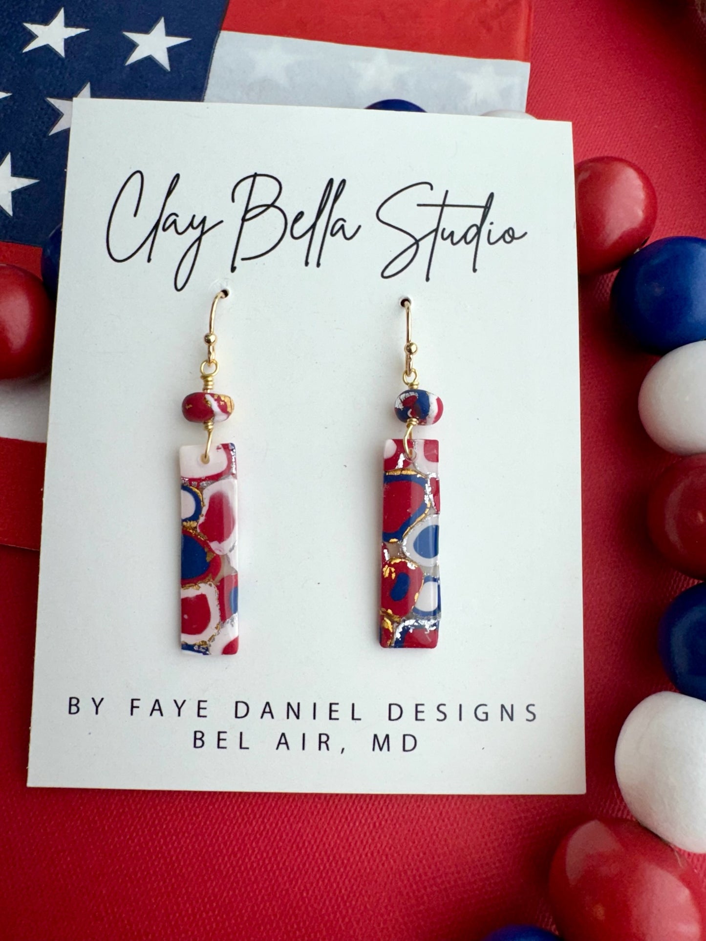 Handmade red, white and blue mosaic polymer clay rectangle earrings with gold and silveer foil. A handmade matching matching bead on Clay Bella Studio display card.