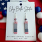 Red, white, and blue striped earrings on a Clay Bella Studio card with American flag in the background.